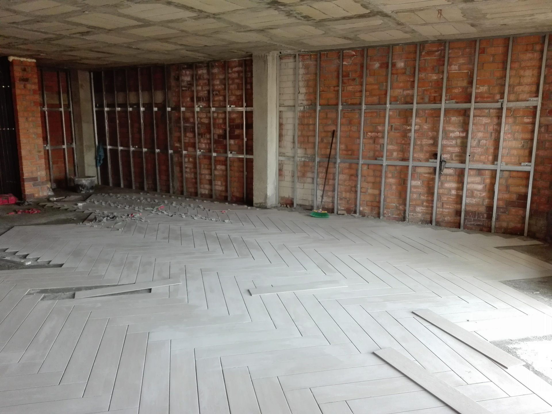 Habitación interior en construcción con paredes de ladrillo visto, montantes metálicos y suelo de madera.