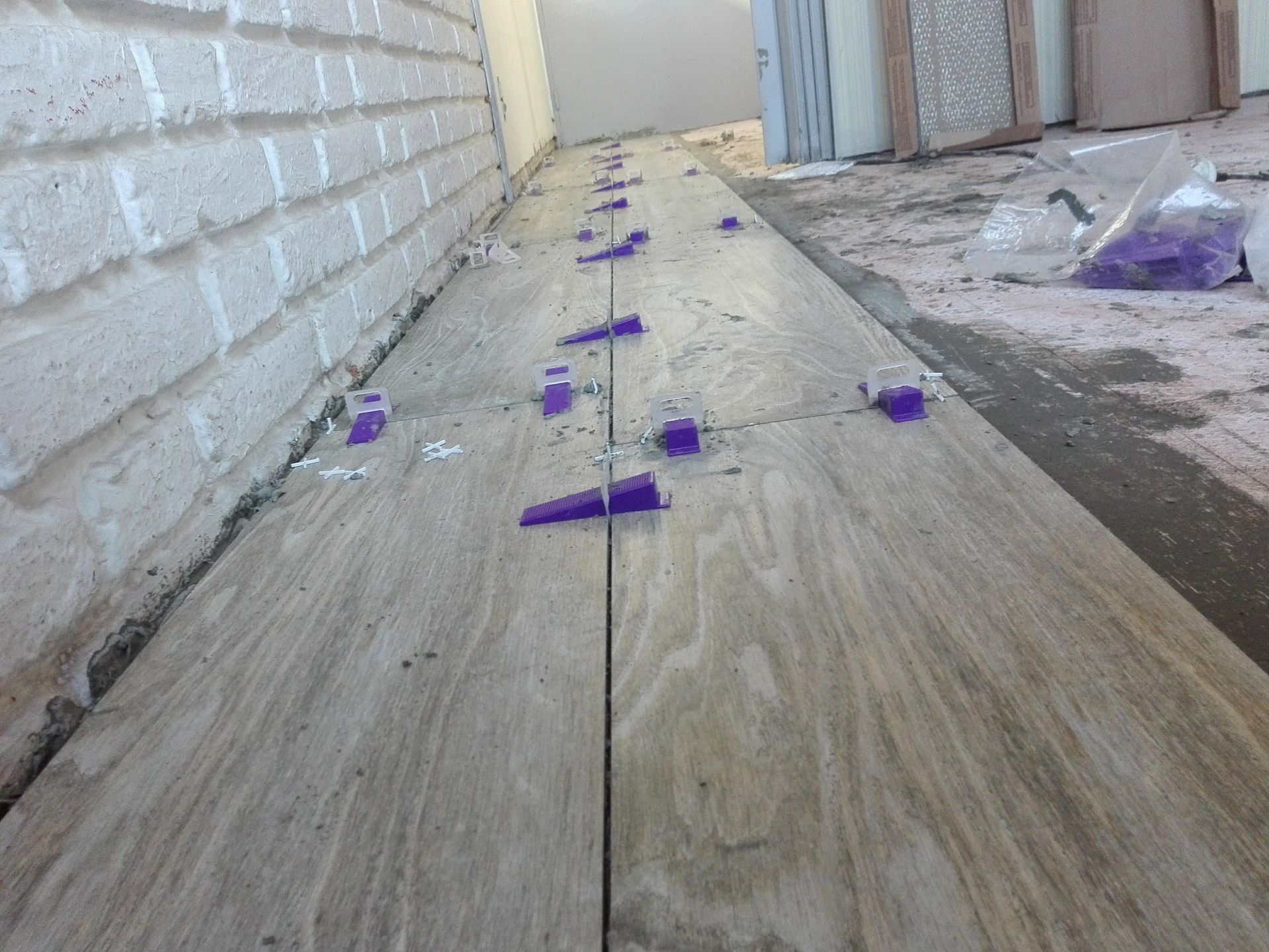 Se están instalando baldosas con clips niveladores morados, cerca de una pared de ladrillo blanco.