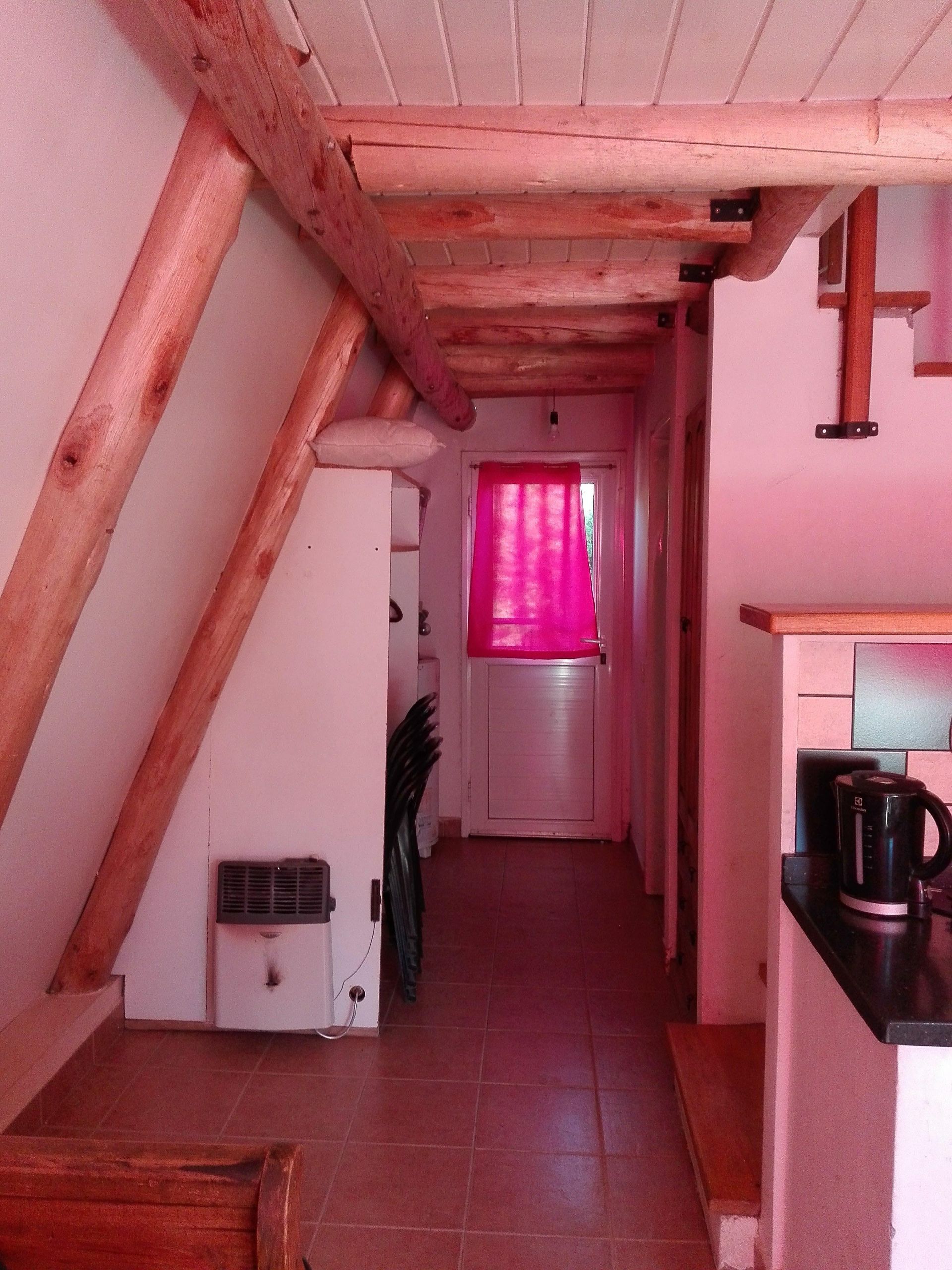 Pasillo interior con vigas de madera, paredes blancas y una cortina rosa.