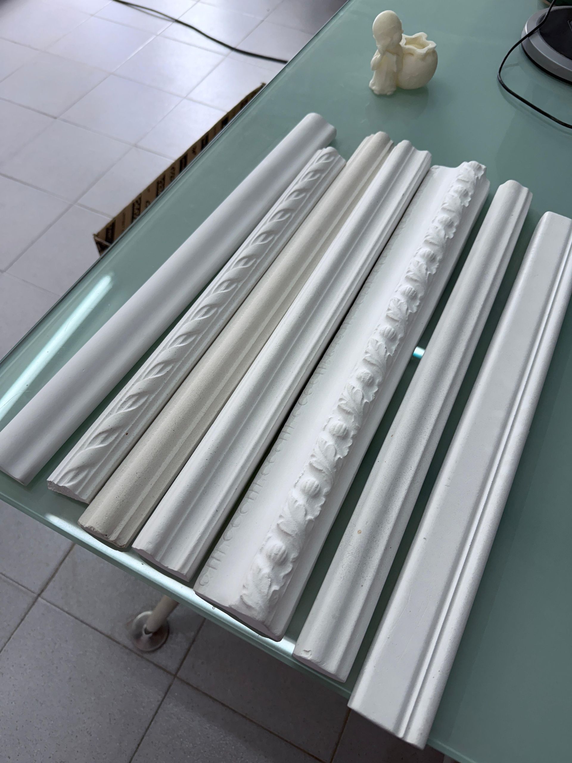 Muestras de molduras blancas expuestas sobre una mesa de cristal.