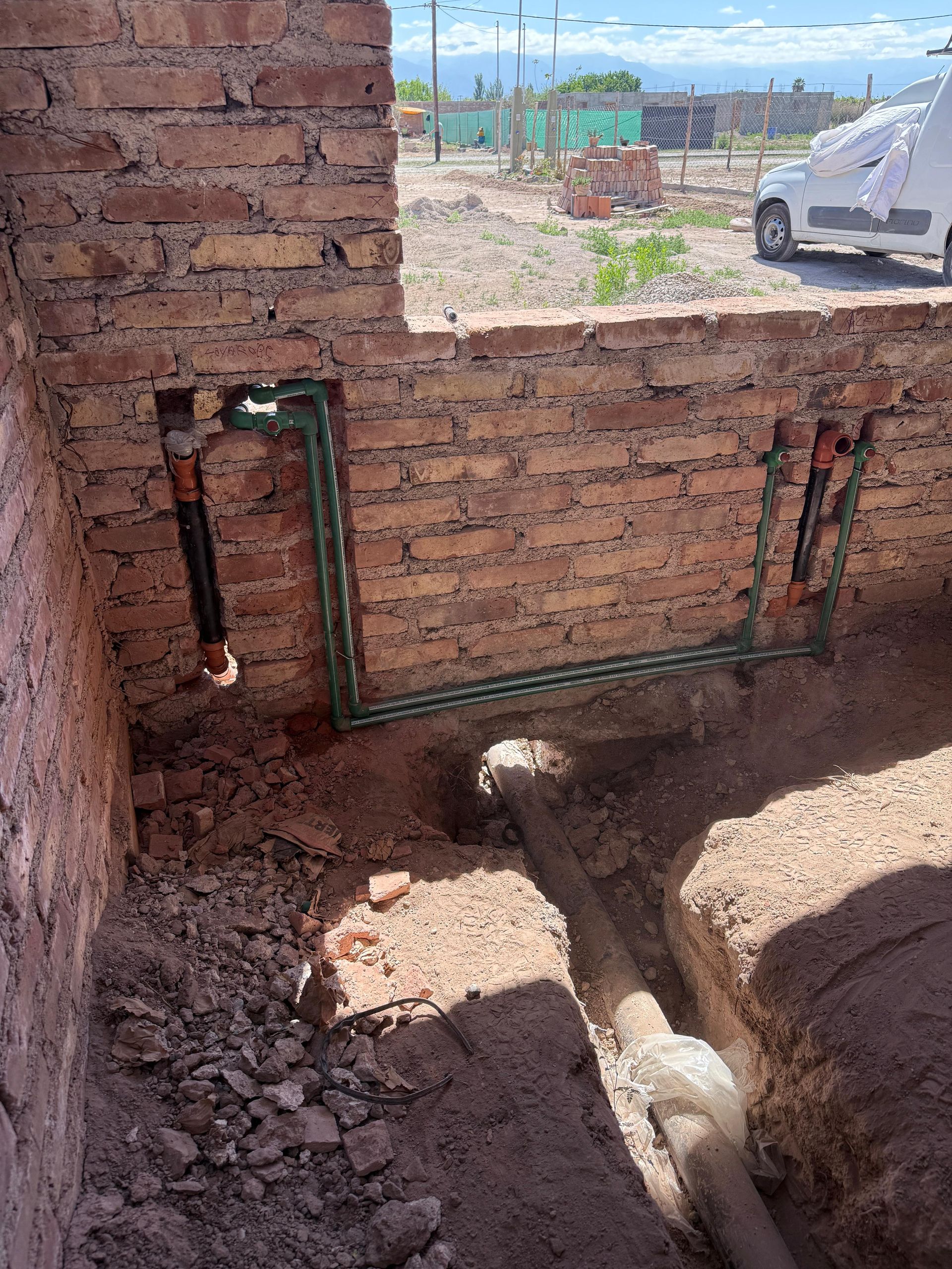 Obra en construcción: tuberías de agua y pared de ladrillo a la vista, luz solar, exterior.
