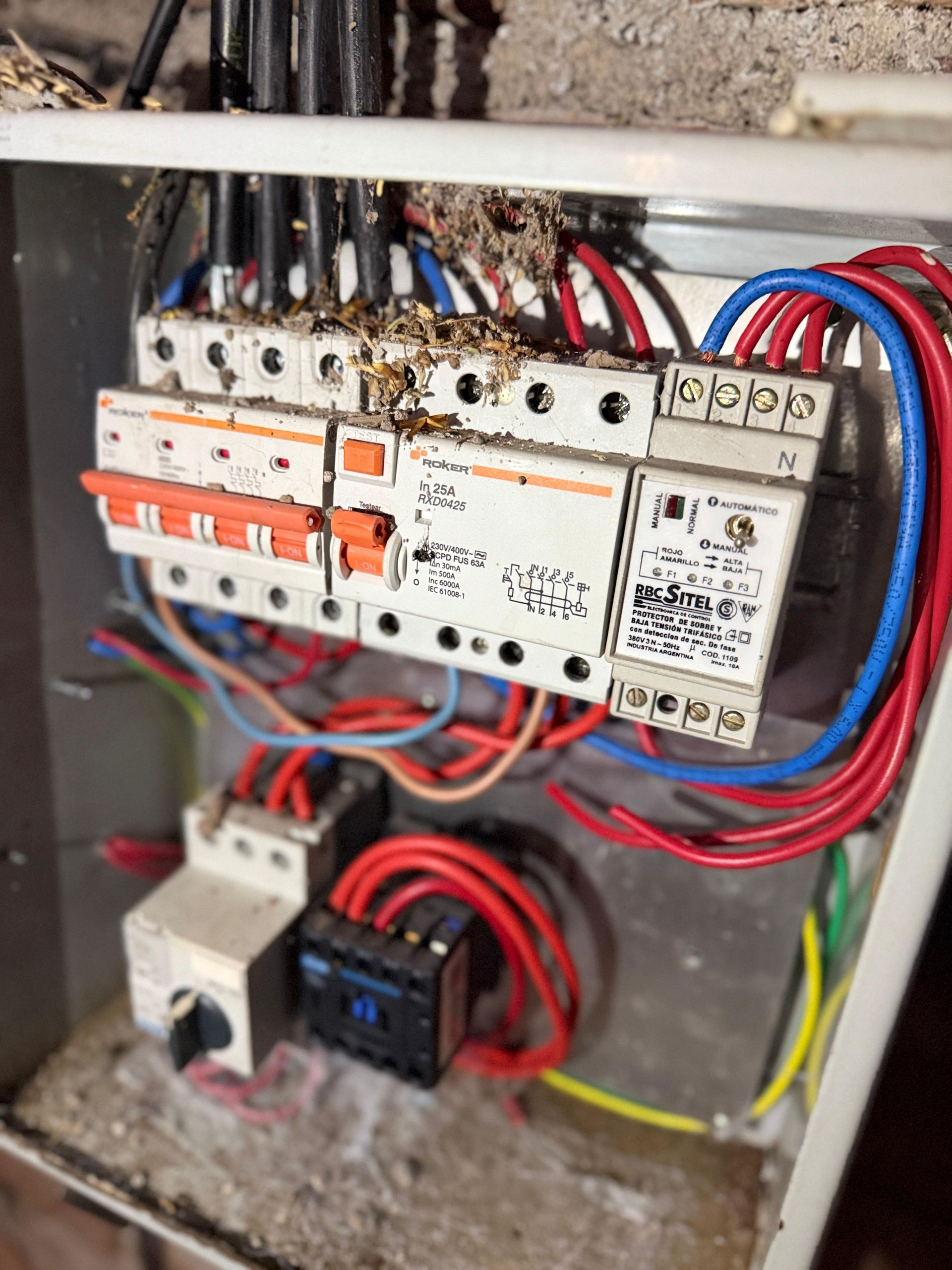 Panel eléctrico con interruptores automáticos naranjas, cables rojos y azules y cables negros, potencialmente dañado.