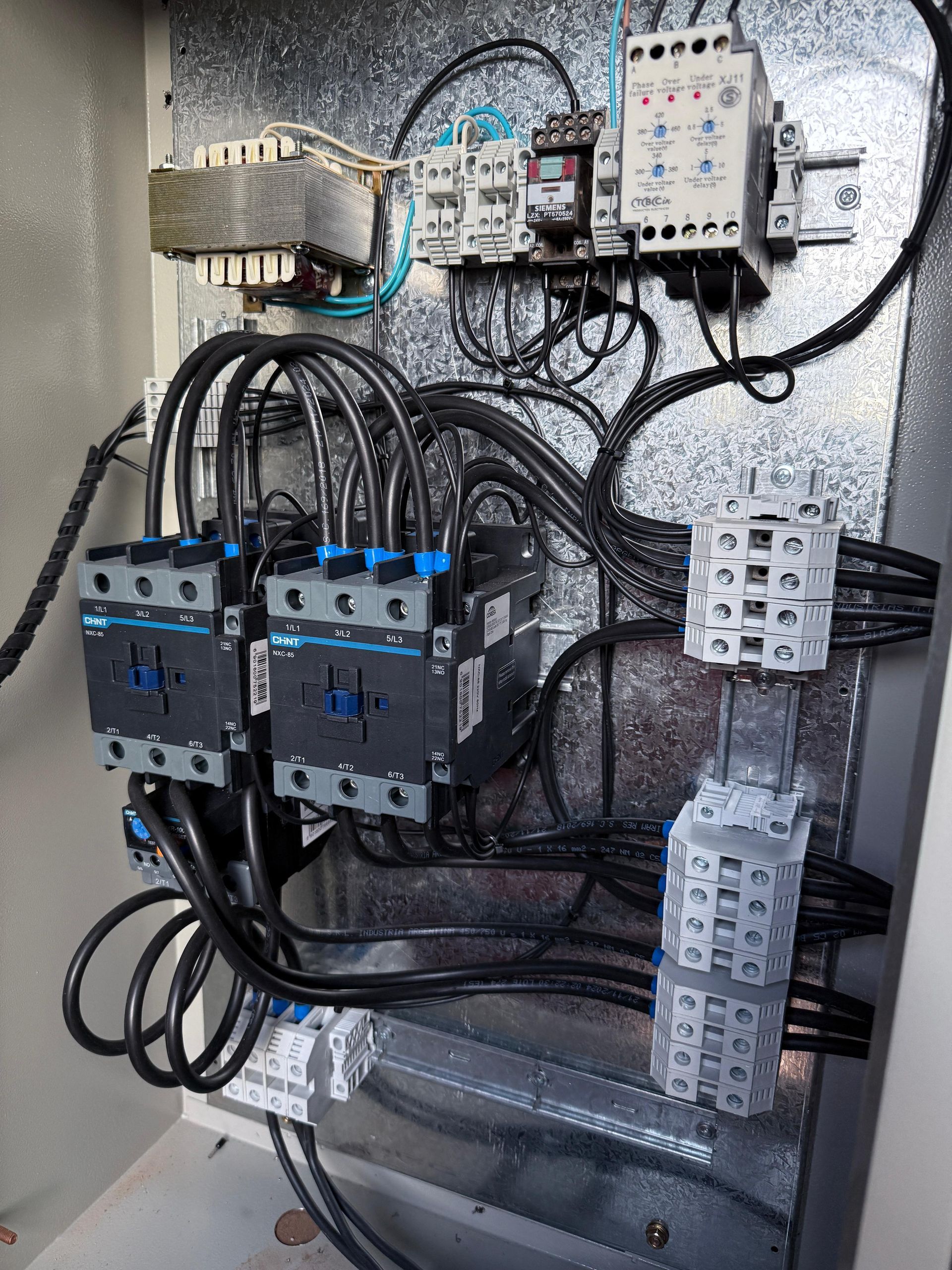 Panel de control eléctrico con cableado negro, contactores y relés.