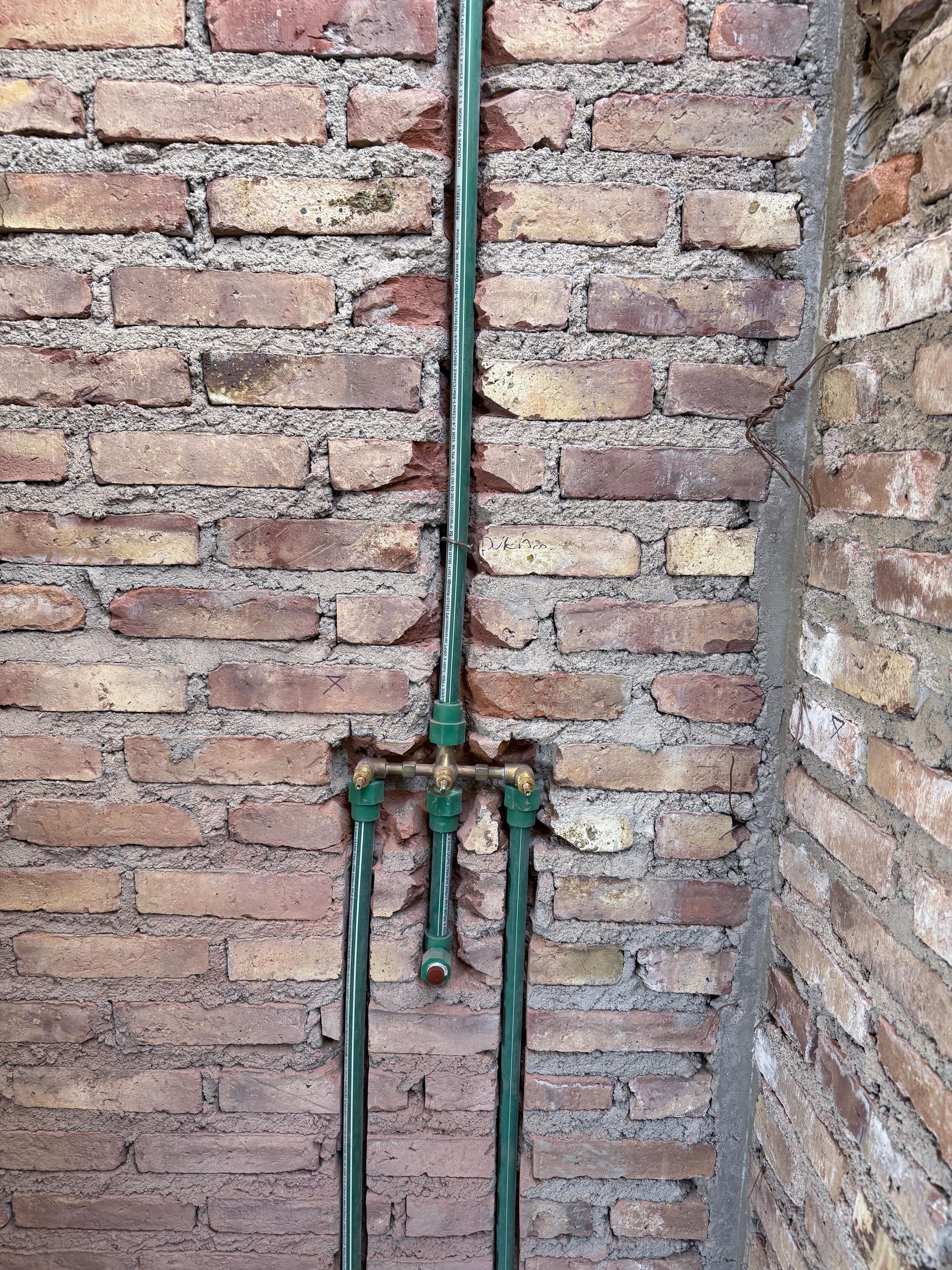 Tuberías verdes en una pared de ladrillo con accesorios de plomería expuestos.