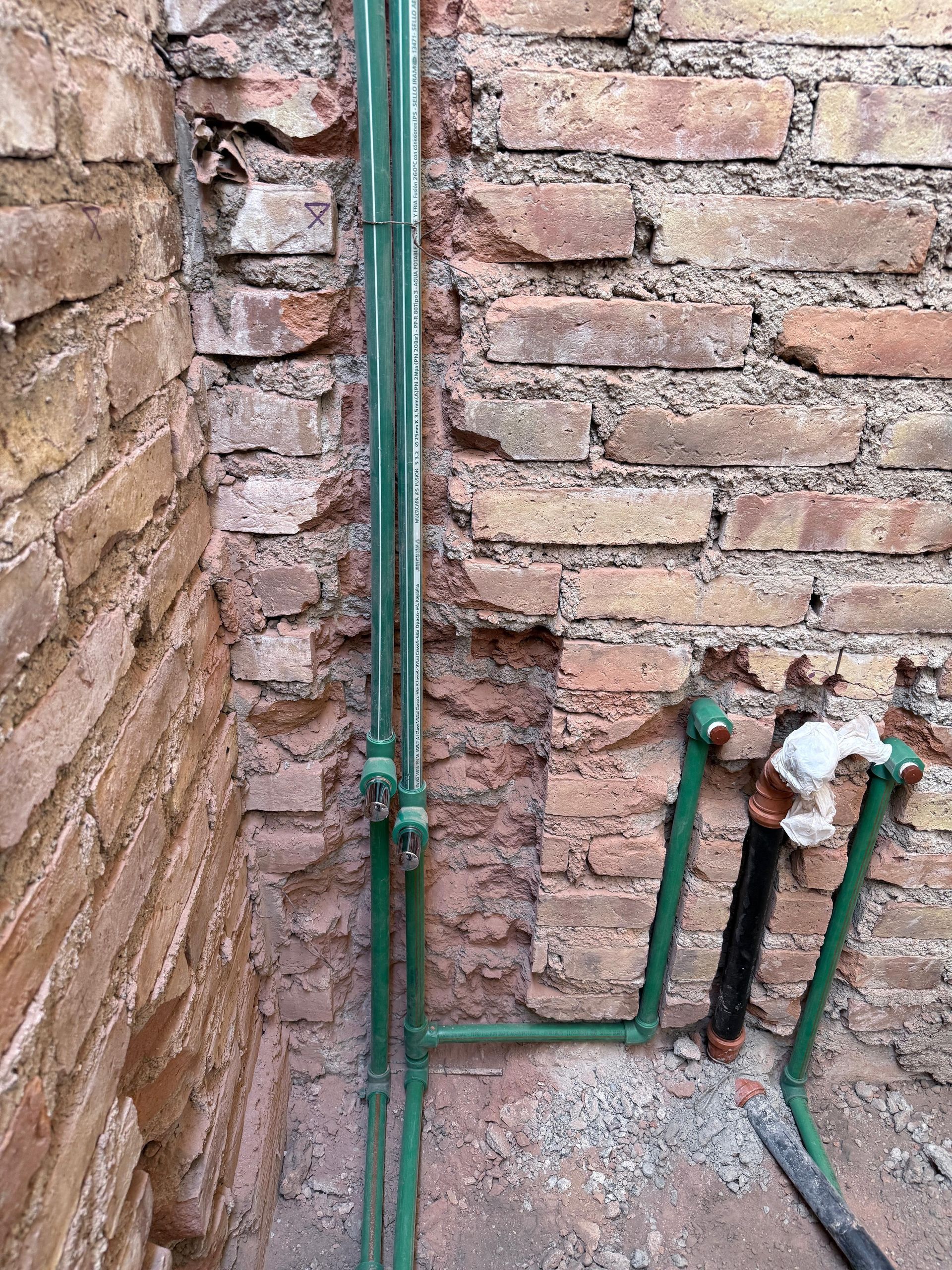 Tuberías verdes en una pared de ladrillo visto. Un grifo está conectado a las tuberías en la parte inferior derecha.