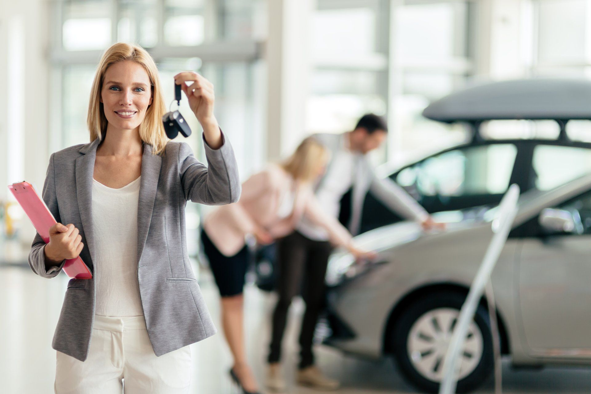 A woman is holding a car key in a car showroom.