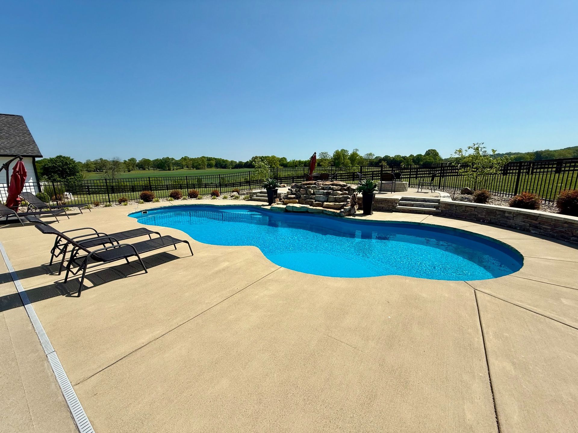 Angled view of a 16x40 backyard pool with stone water feature and patio seating