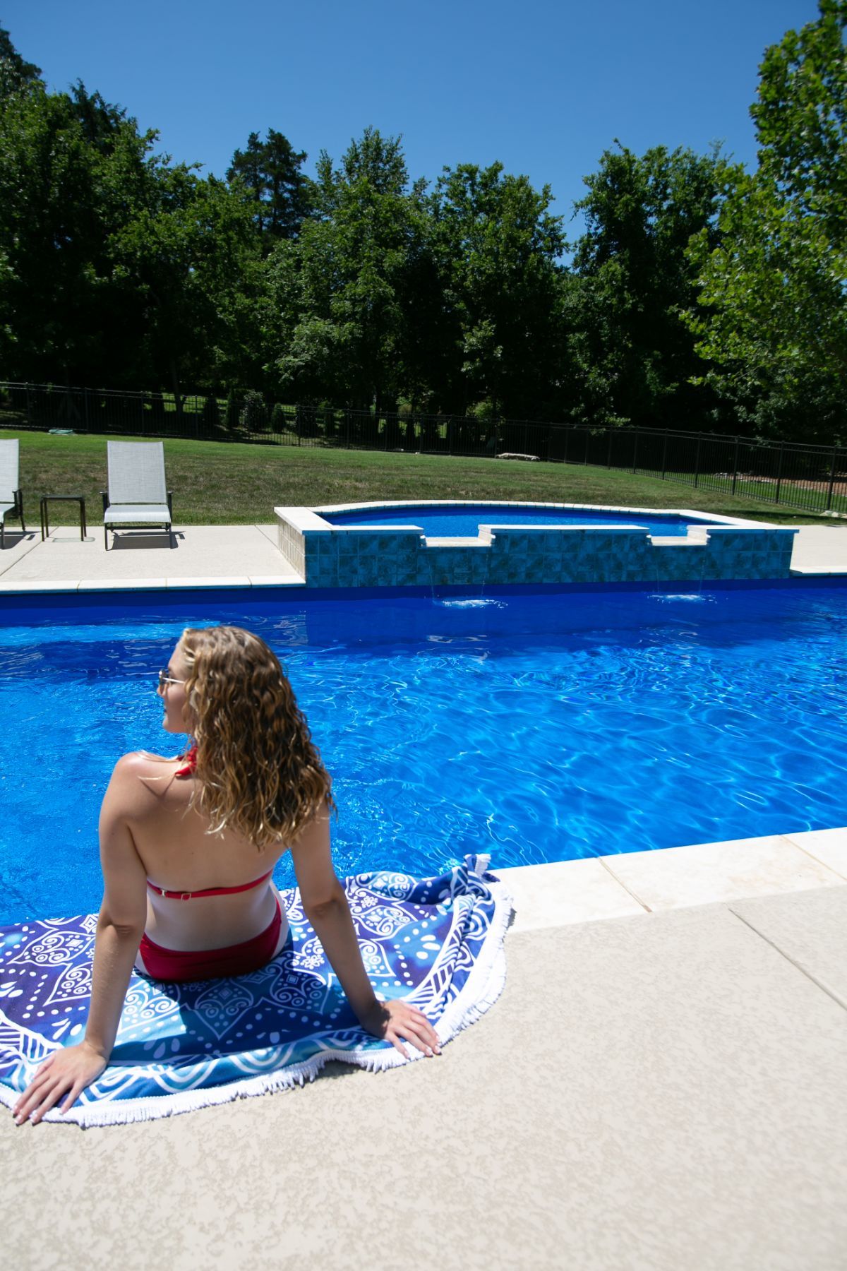 A woman is sitting on a towel near a swimming pool