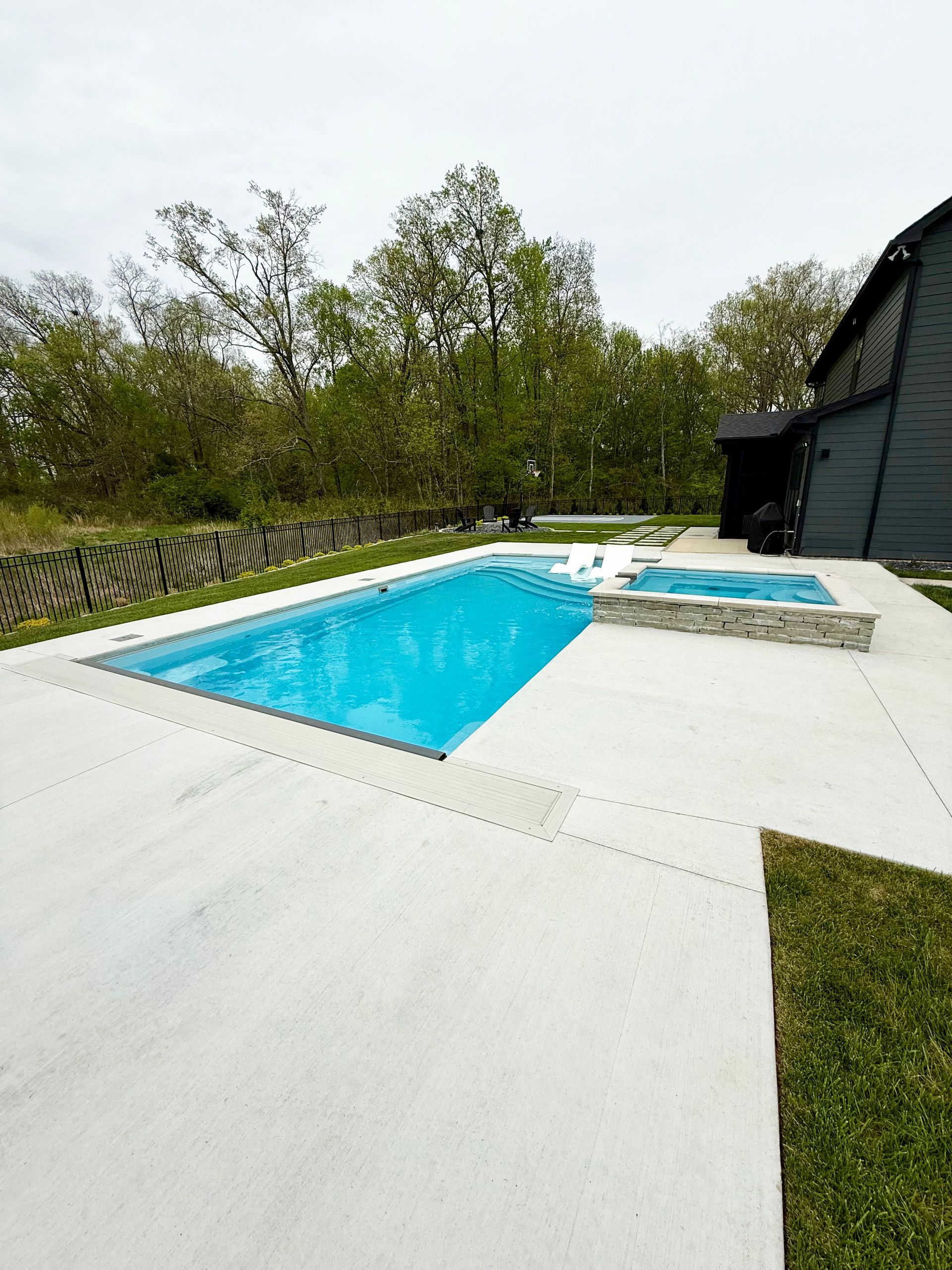 View of the Aspen 16x35 fiberglass pool with attached spillover spa and spacious concrete patio.