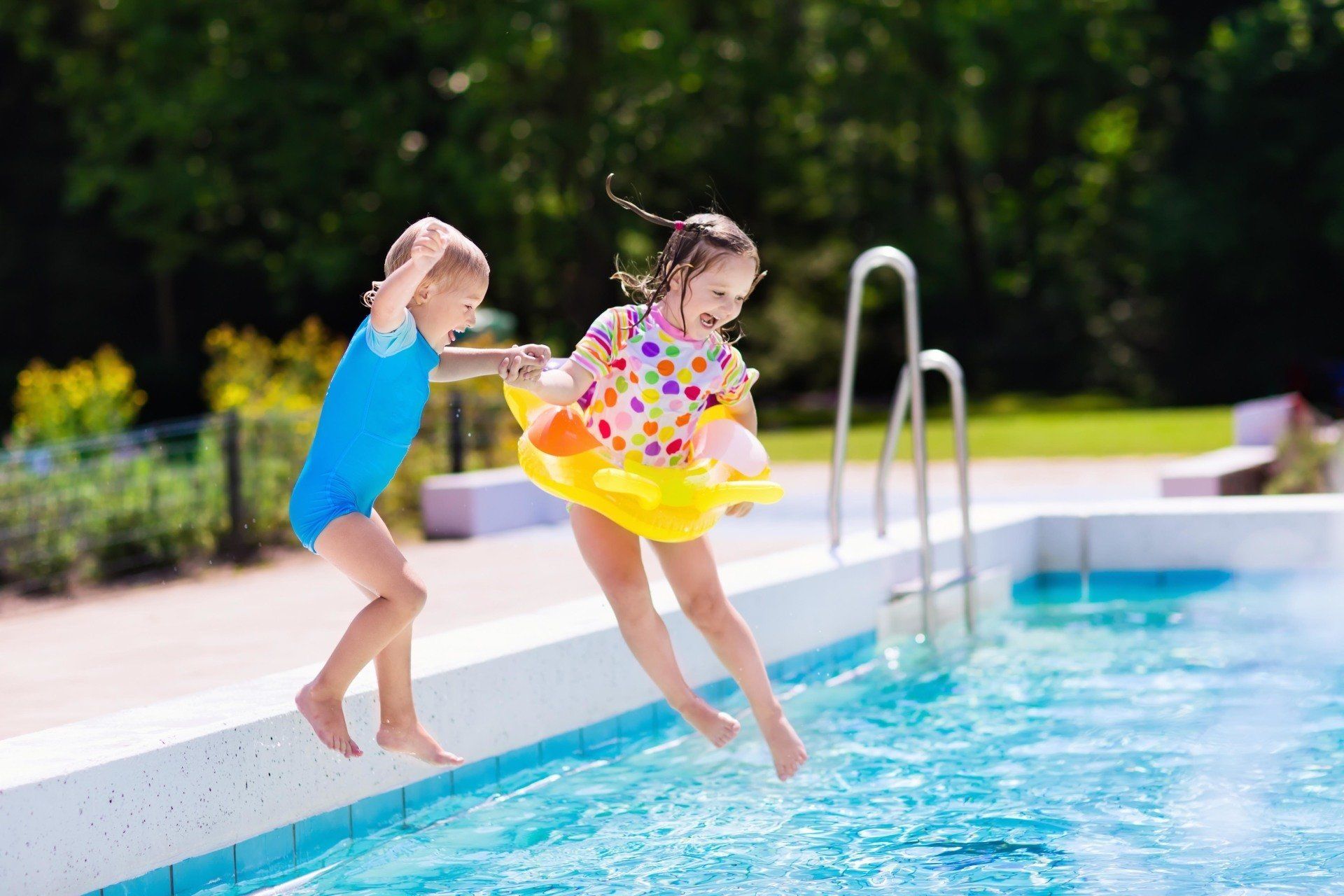 Two little girls are jumping into a swimming pool.