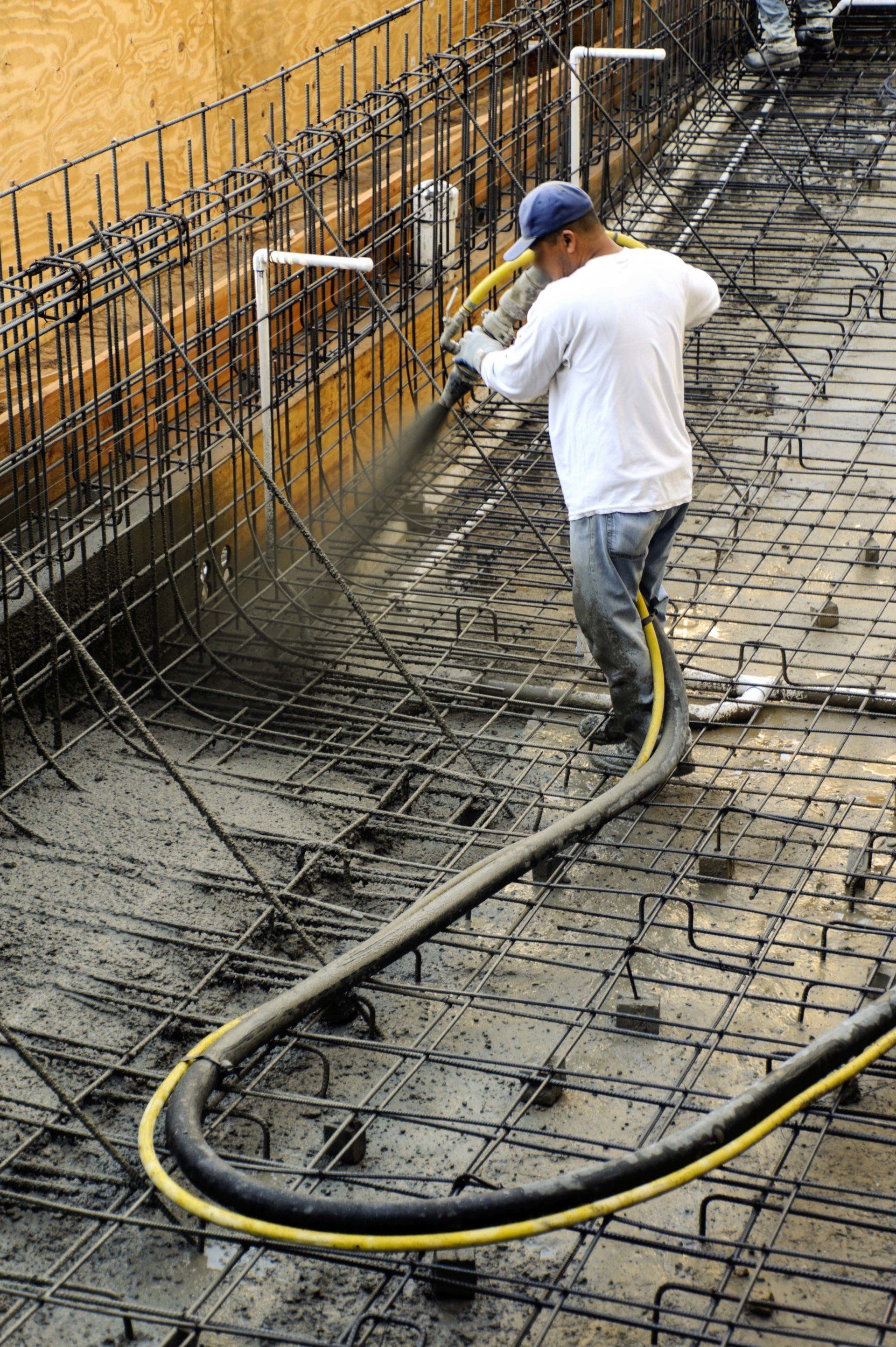 A man is using a hose to pump concrete on a construction site.