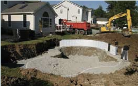A yellow excavator is digging a hole in front of a house.