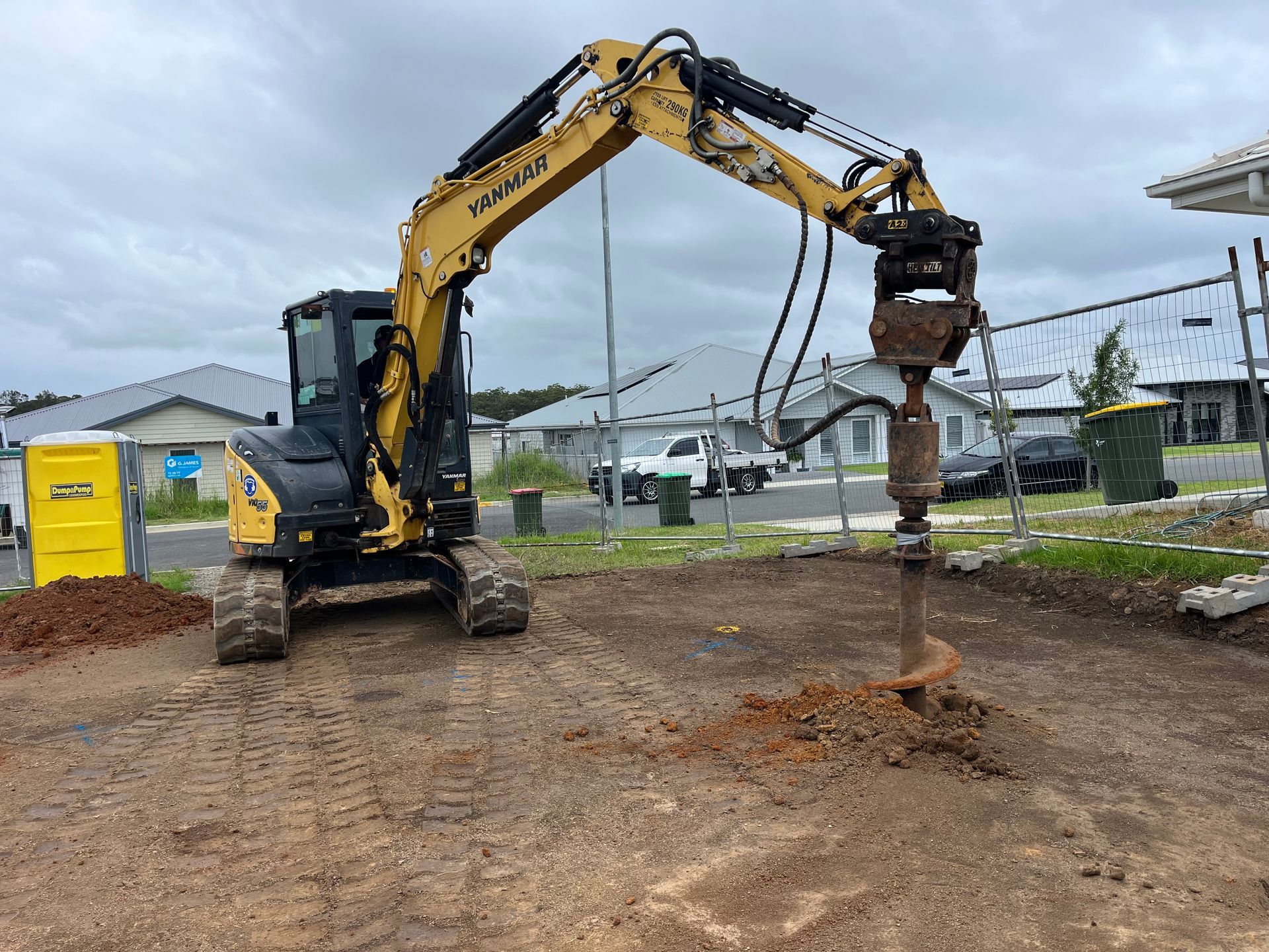 Yellow excavator drilling into the ground on a construction site — Azza's Mini Diggers in Port Macquarie, NSW