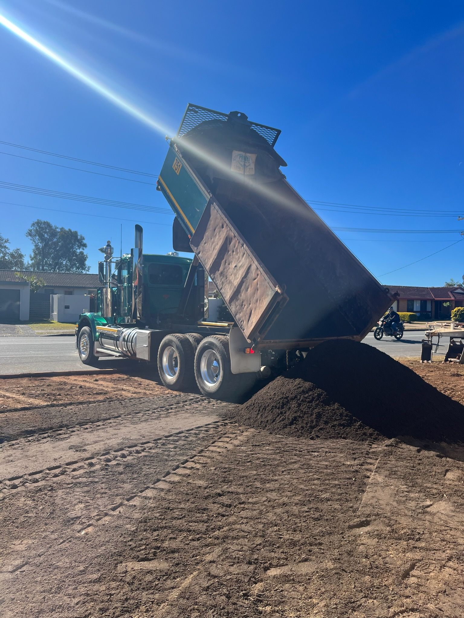 Green dump truck dumping dirt onto a brown surface outdoors under a bright blue sky — Azza's Mini Diggers in Port Macquarie, NSW