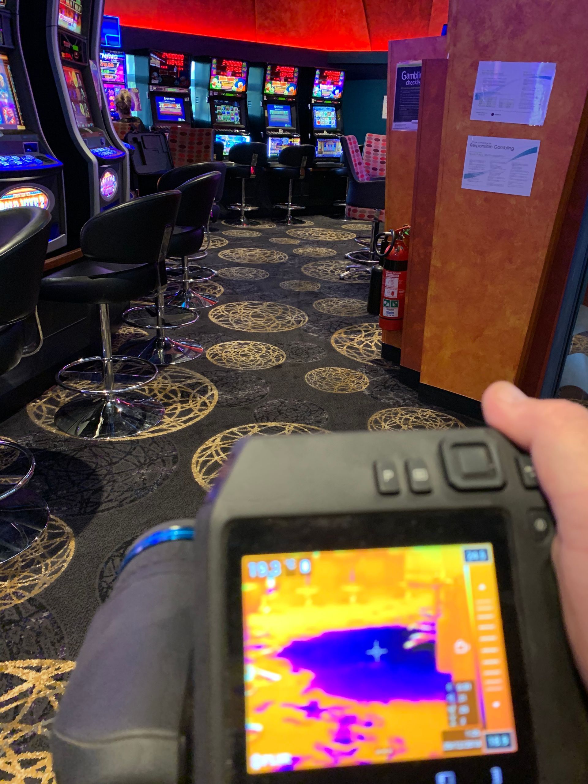 Person holding thermal camera in a casino. Camera shows purple and yellow heat signatures.