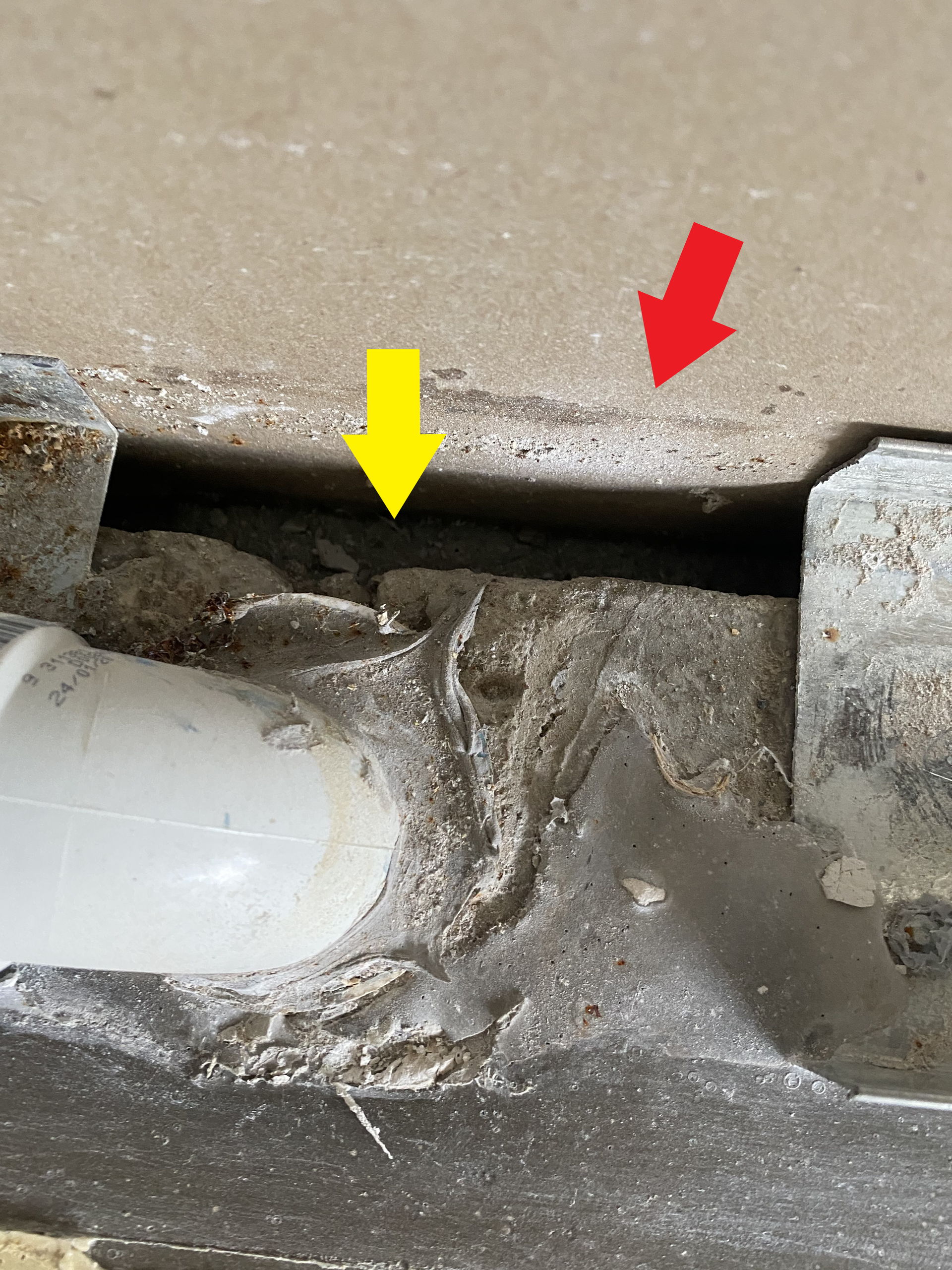 White PVC pipe with debris, cut into a concrete surface, red and yellow arrows point to areas.