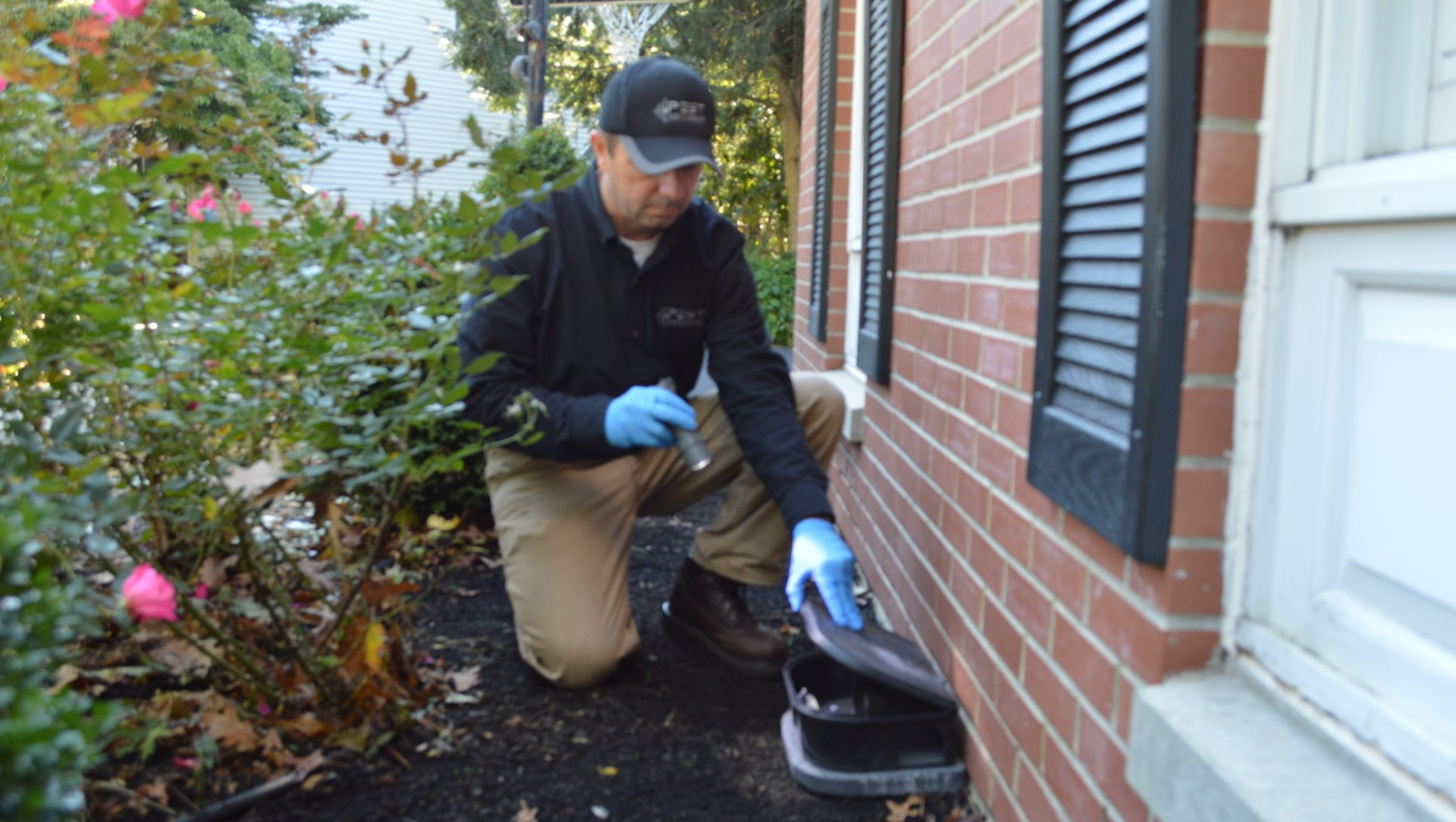 Pest Assassins technician checking an outdoor rodent bait station at customers home in Mansfield, MA