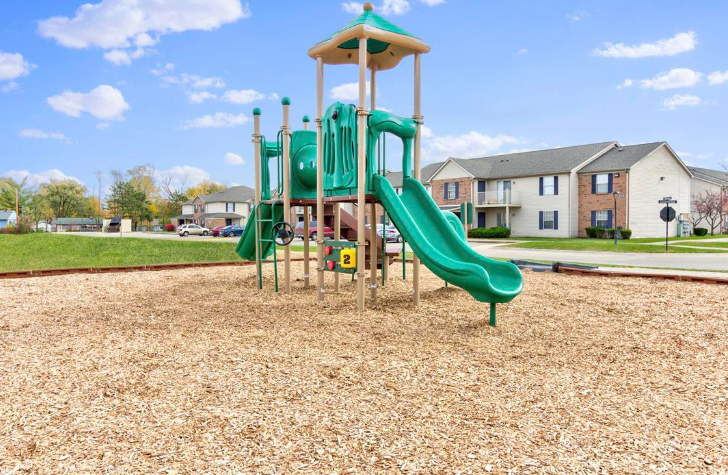 A green playground with a slide and stairs in a park.