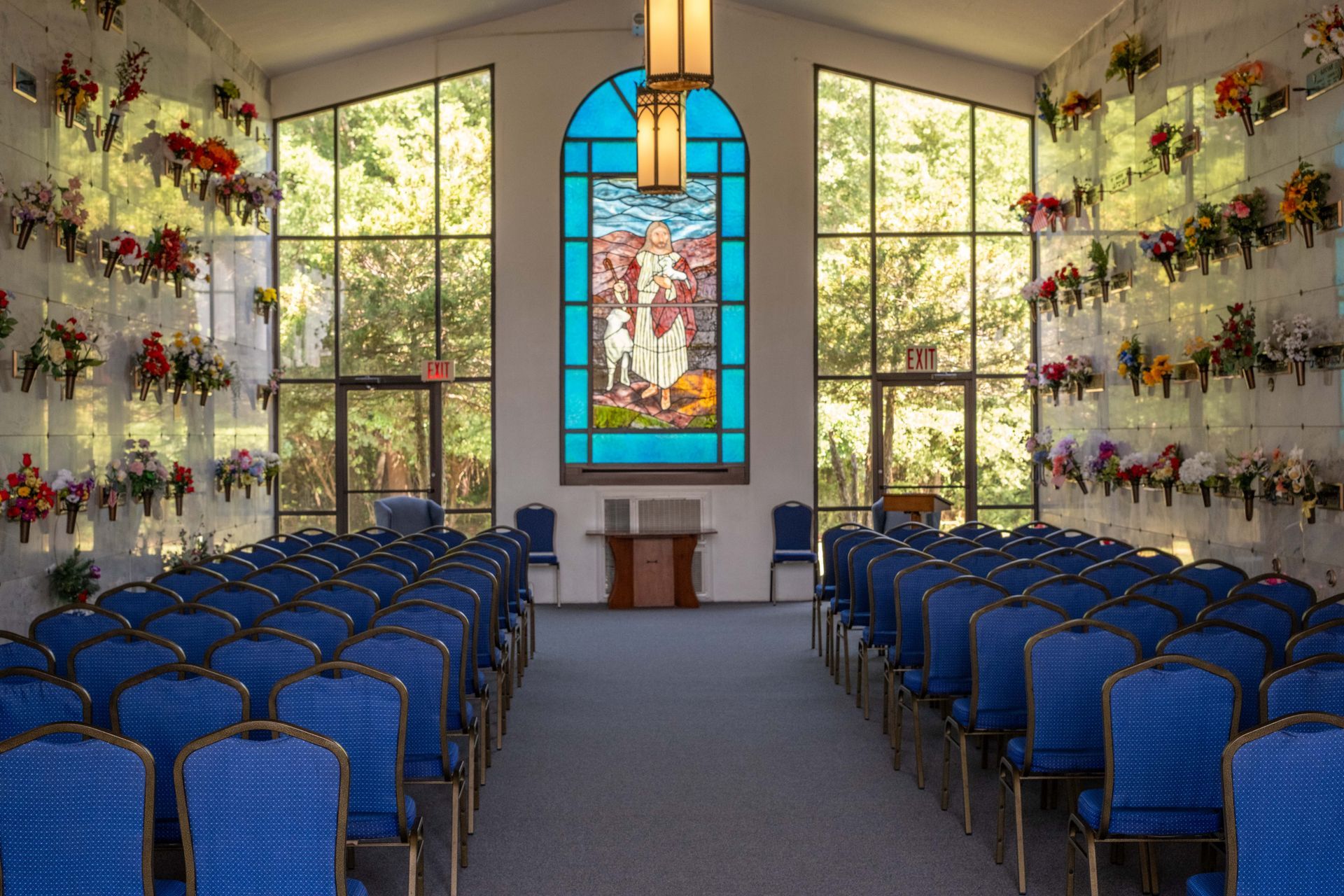 Interior of a mausoleum chapel with blue seating, stained glass, and floral arrangements.