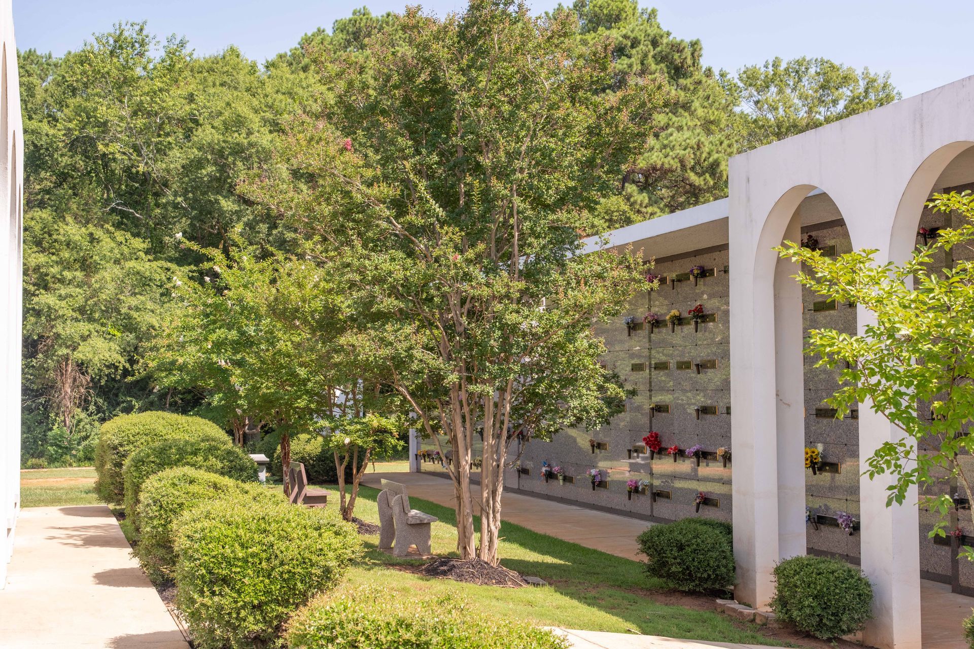 Cemetery with arched walkways, trees, and columbarium walls with niches for urns.