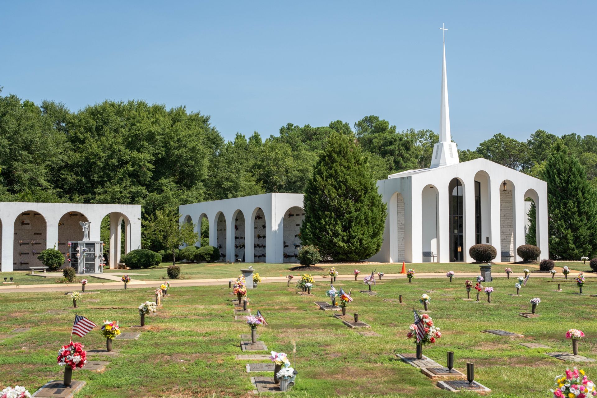 Cemetery with white structures, including a chapel with a steeple, and numerous grave markers under a blue sky.