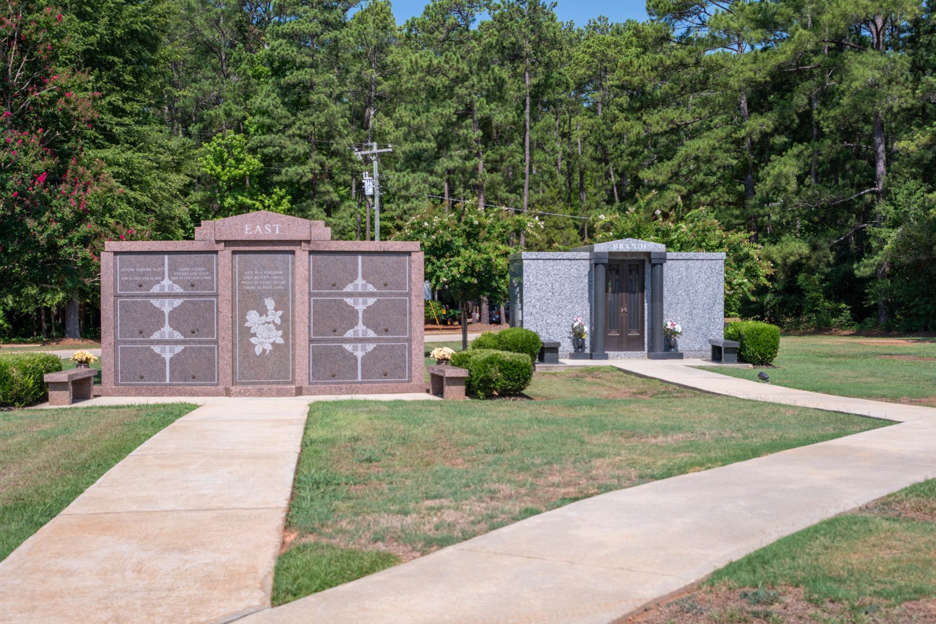 Two mausoleums with paths, set in a grassy area with trees and blue sky.