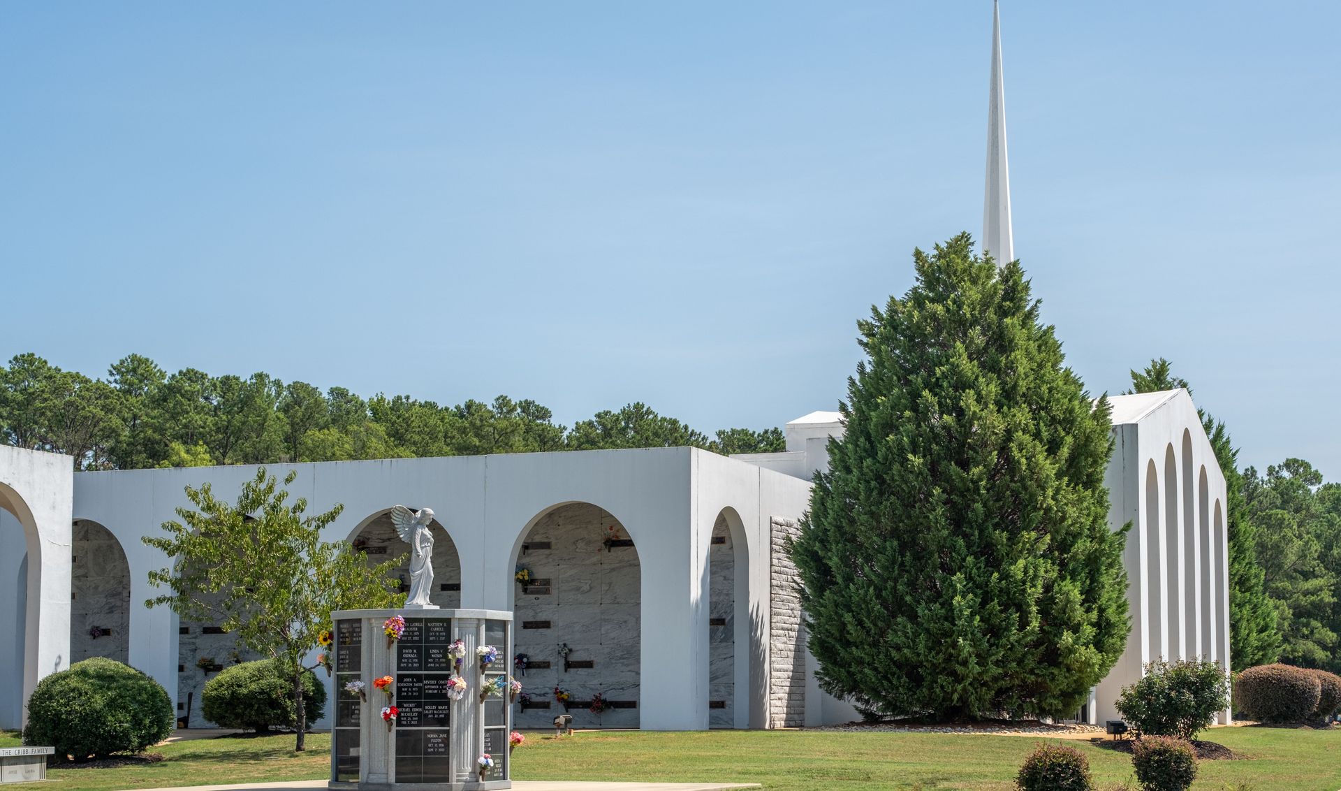 White mausoleum with arched openings and a spire, on a sunny day.