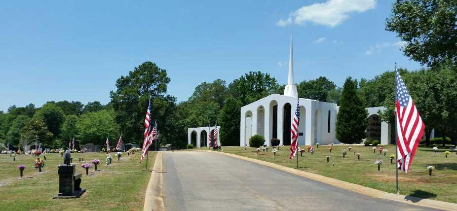 Cemetery with a white building and American flags on a sunny day.