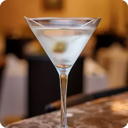 Uma taça de martini com azeitonas está sobre uma mesa.