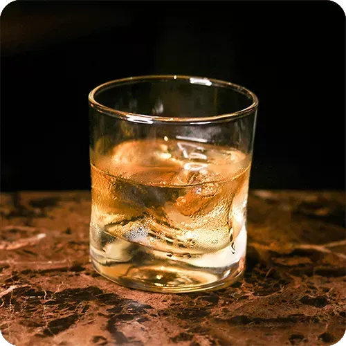 Um copo de whisky com cubos de gelo sobre uma mesa.