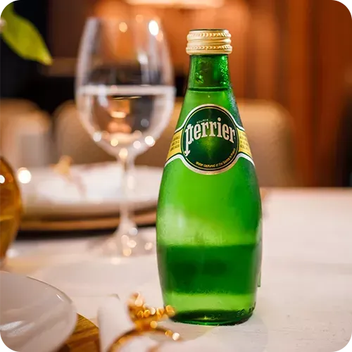 Uma garrafa de água Perrier está sobre uma mesa ao lado de um copo d'água.