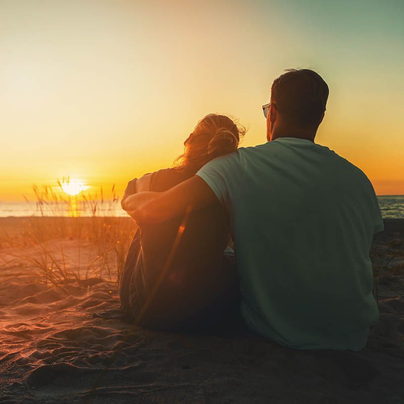 Casal abraçado assistindo ao pôr do sol na praia.