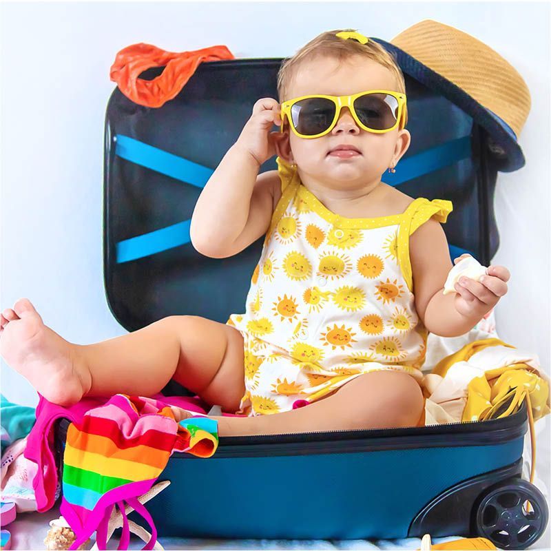 Bebê feliz com óculos em mala pronta para viagem.