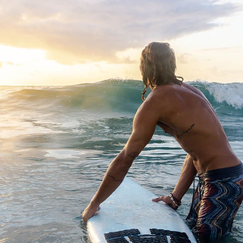 Surfista contempla onda ao pôr do sol.