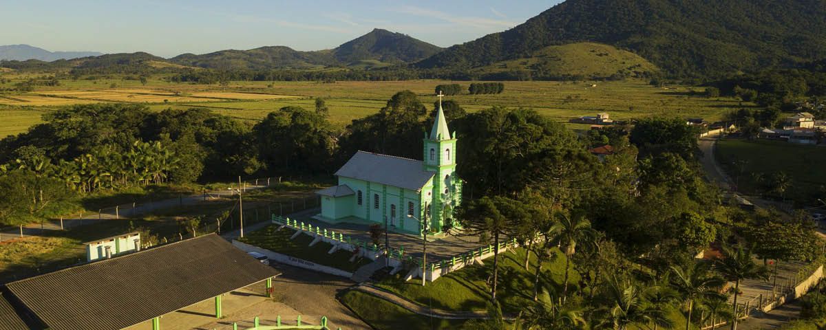 Uma vista aérea de uma igreja verde cercada por árvores e montanhas.