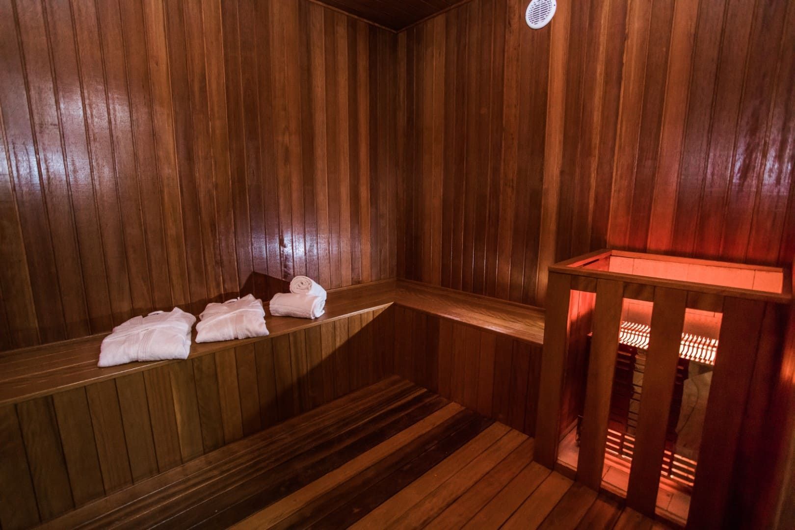 Sauna de madeira com toalhas nos bancos e luz vermelha.