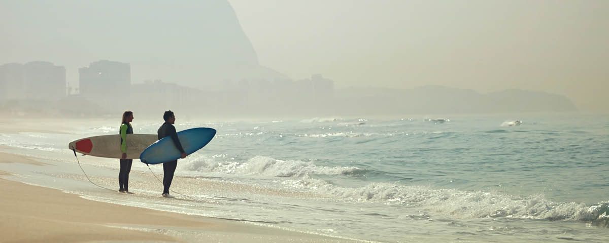Dois surfistas estão na praia segurando pranchas de surf.