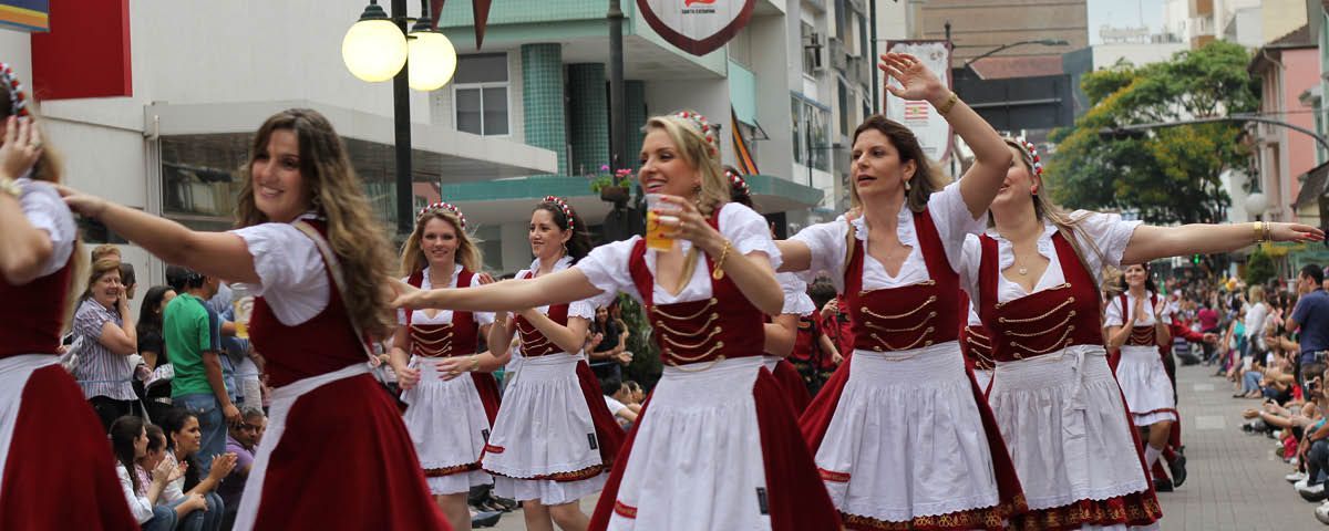 Um grupo de mulheres em trajes tradicionais alemães dança em desfile.