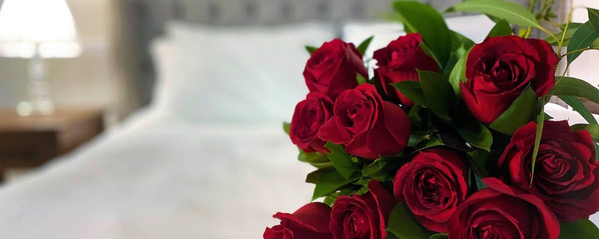 Um buquê de rosas vermelhas está sobre uma mesa em frente à cama.
