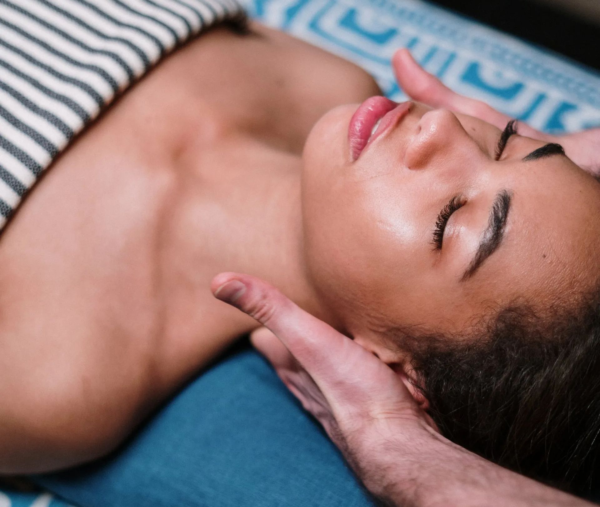 Uma mulher deitada na cama com os olhos fechados recebendo uma massagem