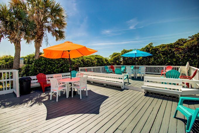 A deck with tables , chairs , and umbrellas on a sunny day.