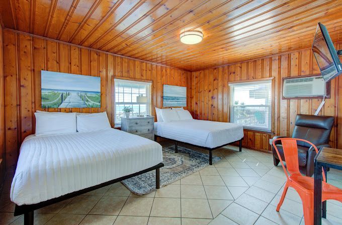 A hotel room with two beds , a chair and a table.