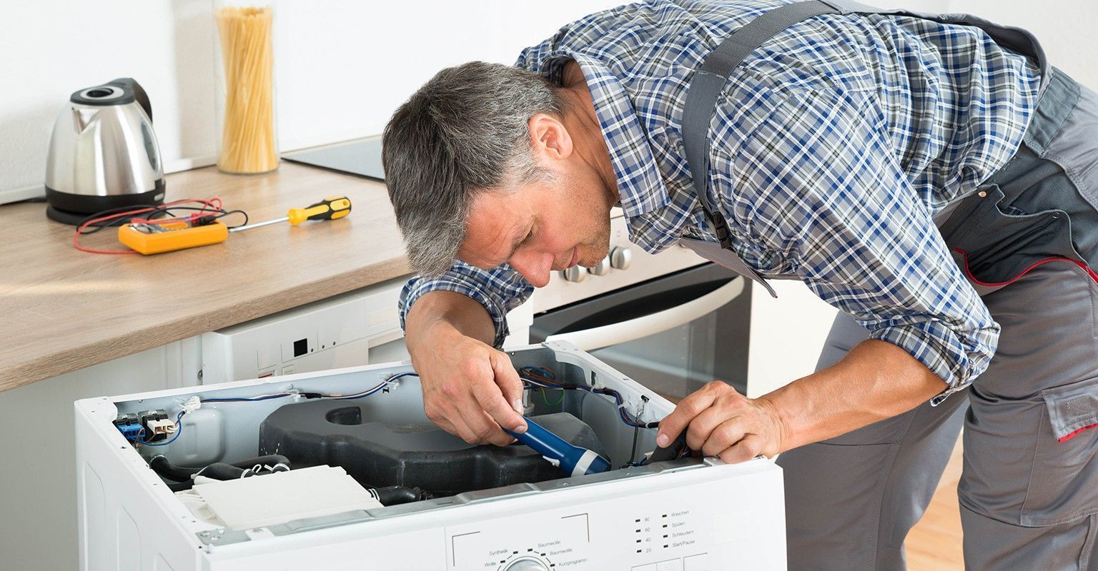 A man is working on a washing machine in a kitchen.
