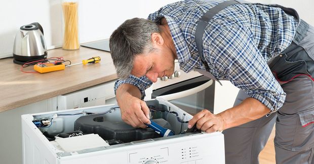 A man is working on a washing machine in a kitchen.