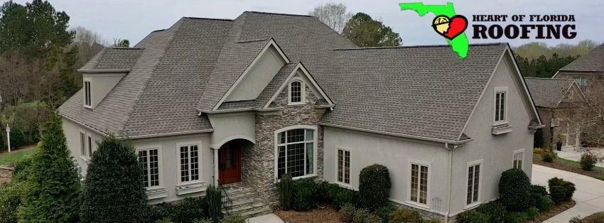 A large white house with a heart of florida roofing logo on the roof.