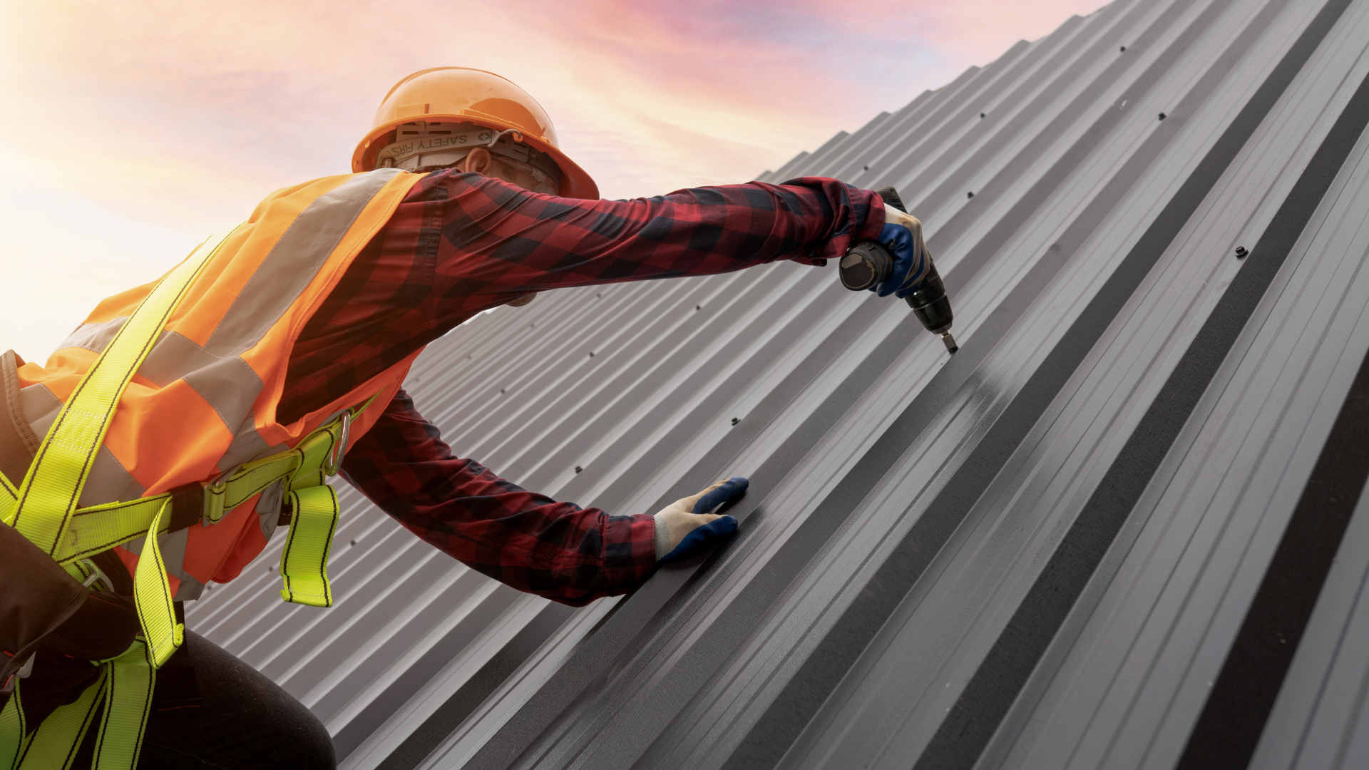 A man is working on a metal roof with a drill.
