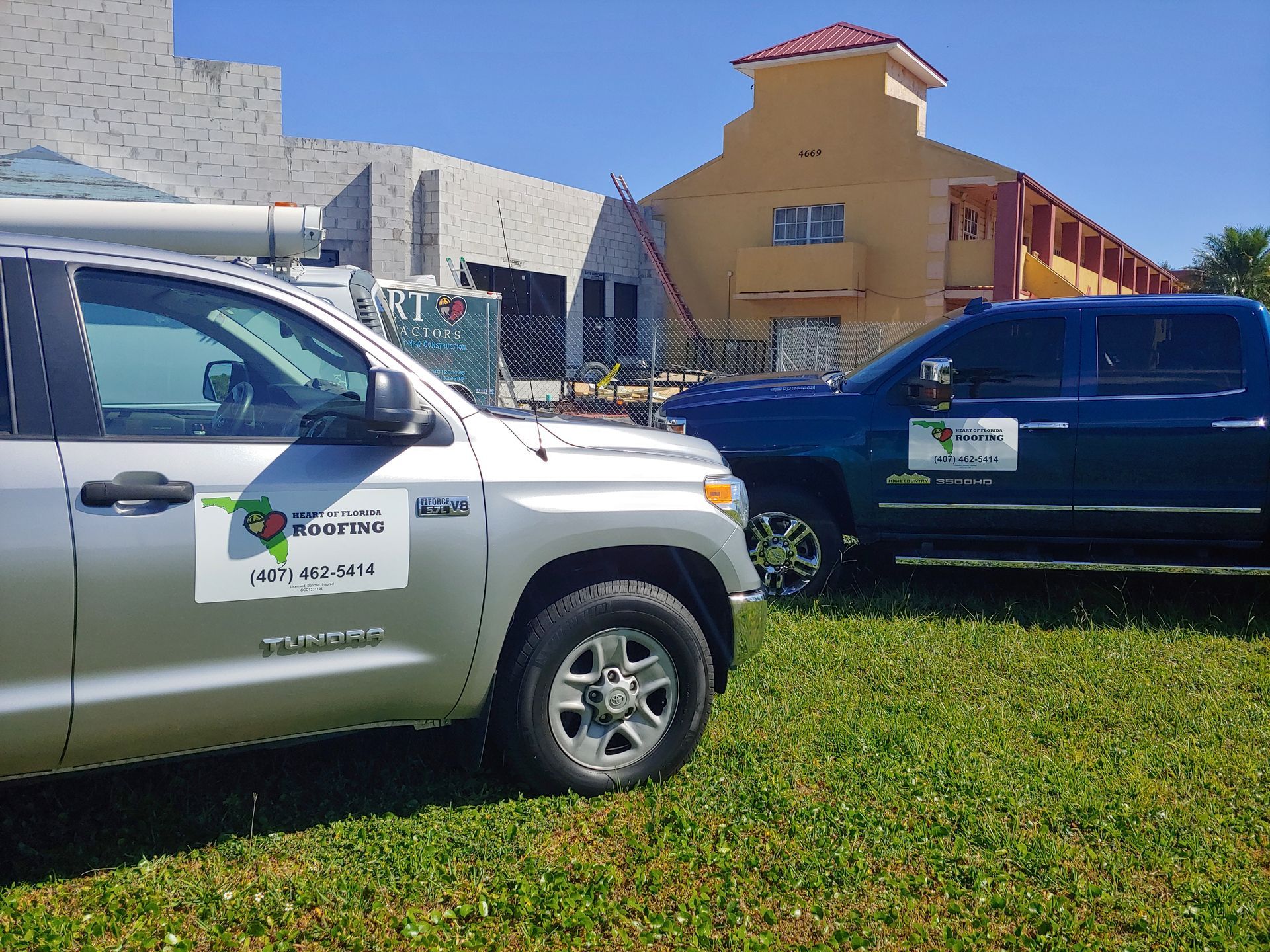 Two trucks are parked in a grassy field in front of a building.