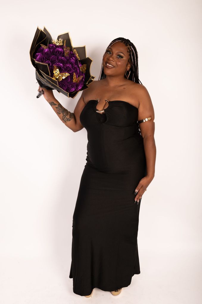 A woman in a black dress is holding a bouquet of purple flowers.