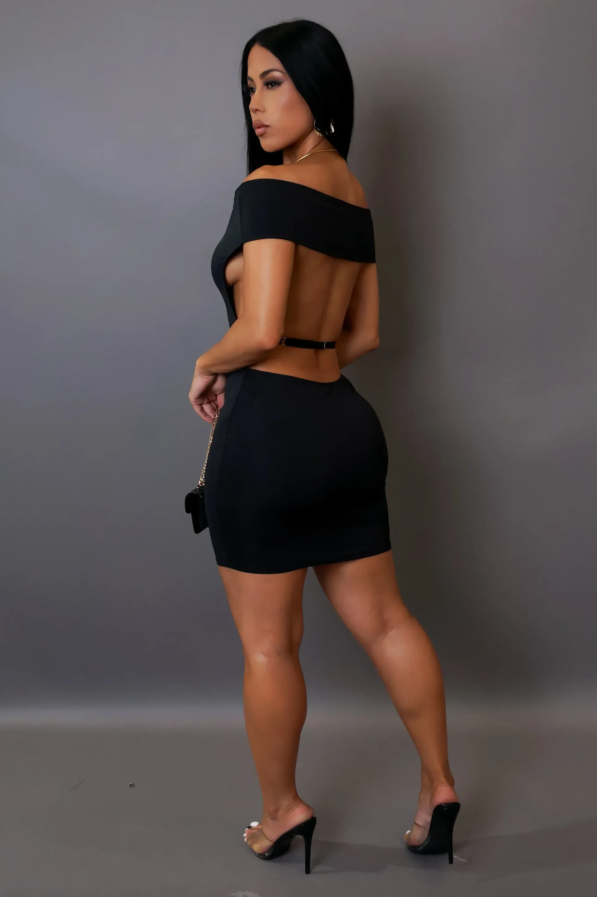 A woman is wearing a black off the shoulder dress and holding a purse.