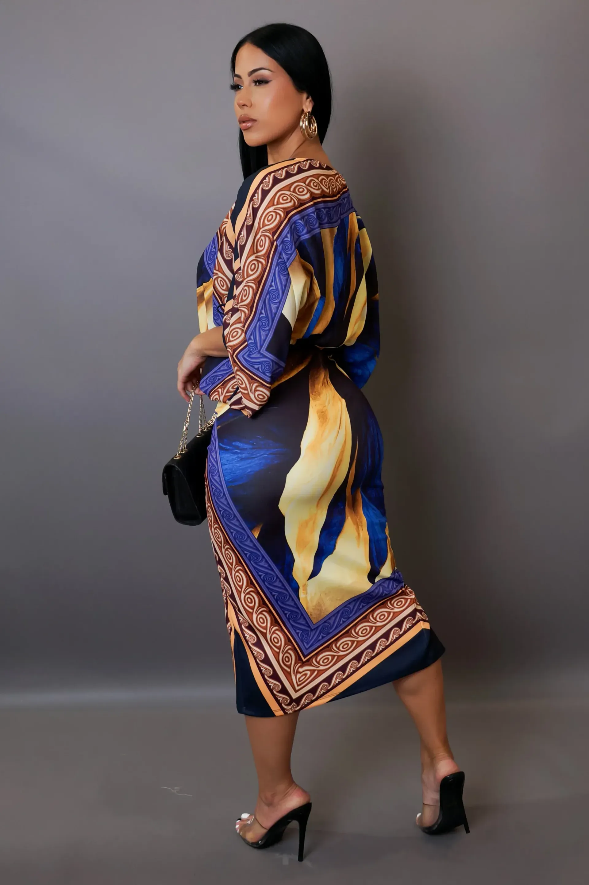 A woman is wearing a colorful dress and holding a black purse.